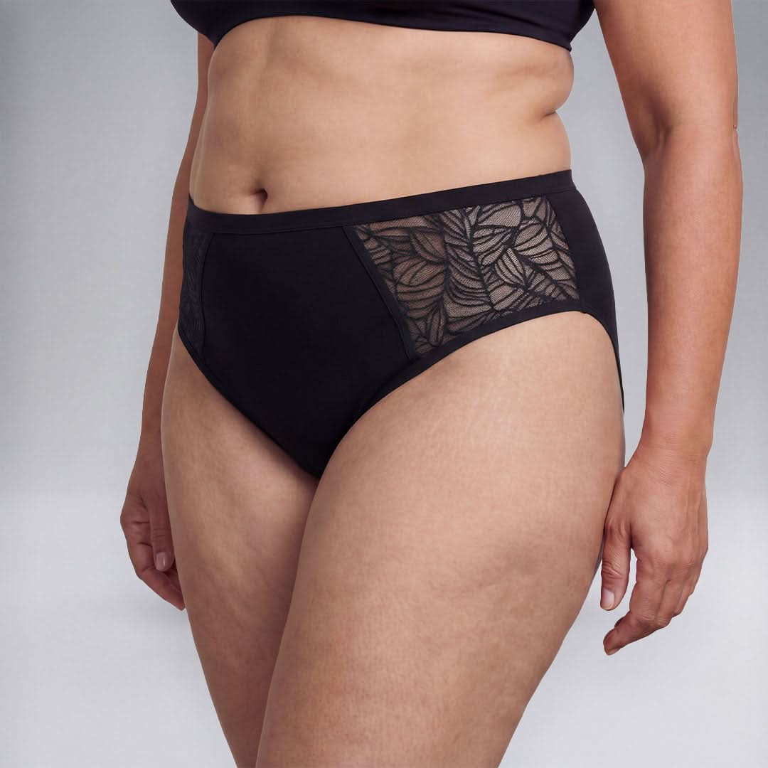 Woman wearing black absorbent underwear with lace side panels, washable and discreet solution for female incontinence, providing breathable and comfortable protection against light to moderate bladder leaks.