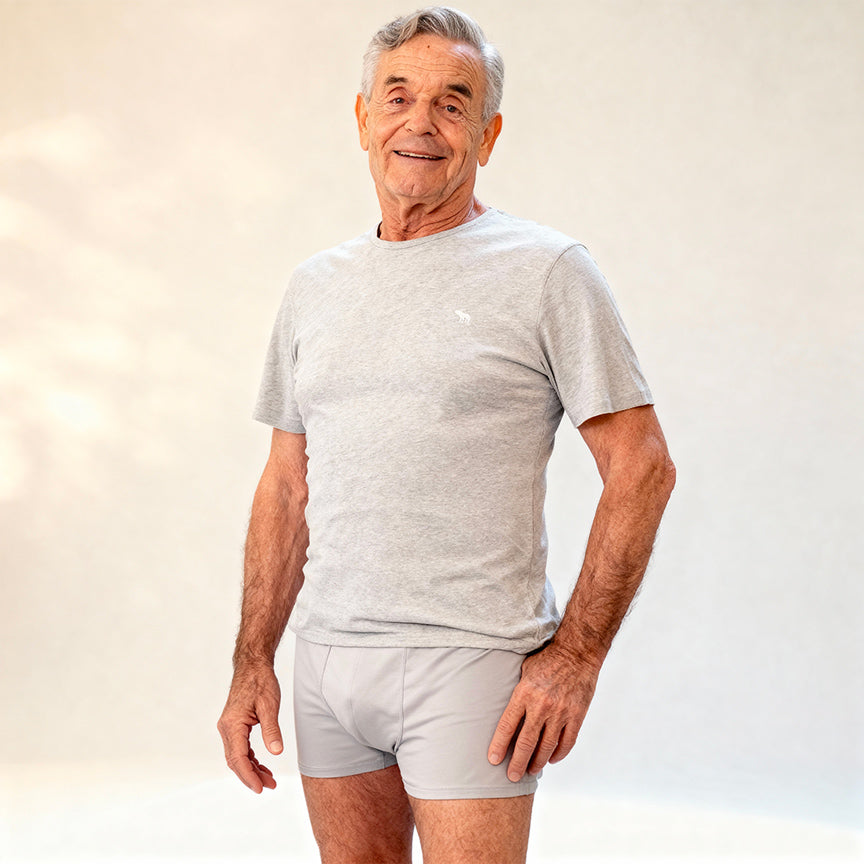Senior man wearing a light gray Orykas absorbent boxer with a t-shirt, showcasing a discreet and comfortable underwear designed for light to moderate bladder leaks, providing invisible protection and freedom of movement every day.