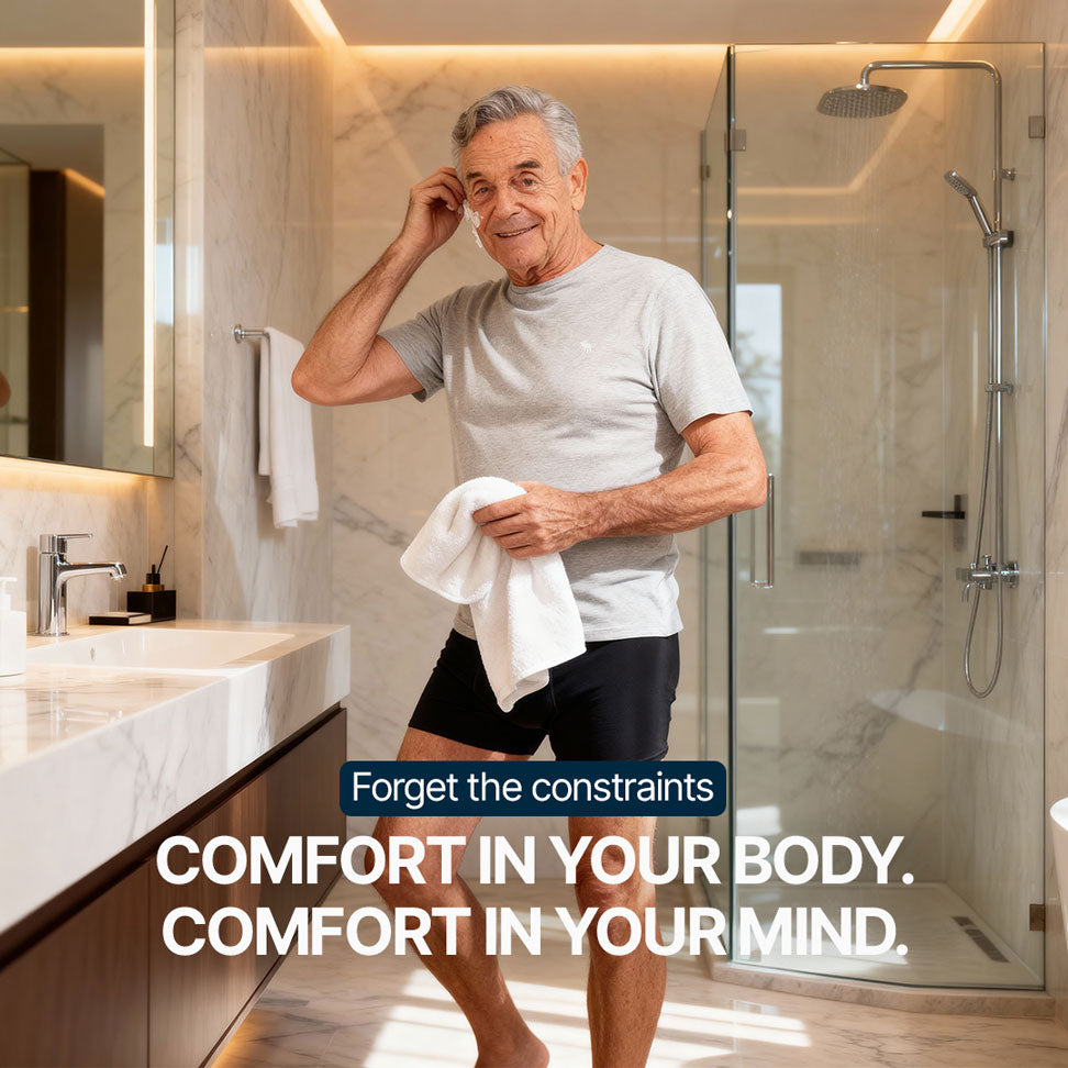 Senior man wearing black Orykas absorbent boxer briefs in a bright bathroom, holding a towel and smiling, illustrating washable and discreet underwear designed to live freely despite light to moderate bladder leaks.