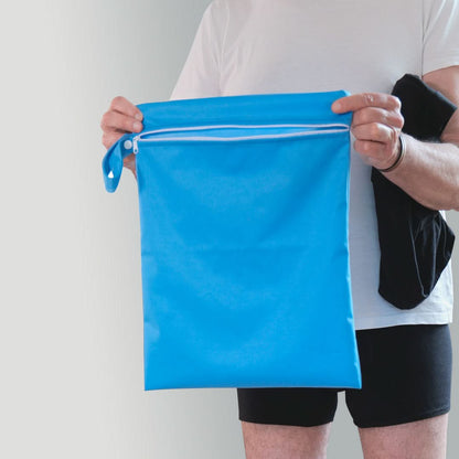 Man holding a blue Orykas waterproof bag with a zipper, designed to discreetly carry absorbent underwear for bladder leaks, a practical and water-resistant accessory for travel and daily use.